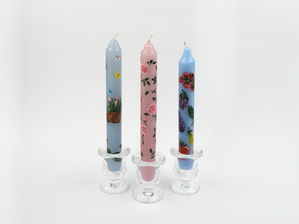 Three colorful candles with hand painted floral designs in glass candle holders on a white background