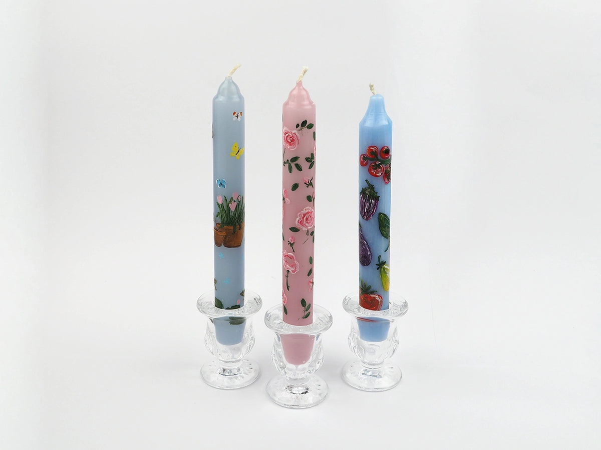 Three colorful candles with hand painted floral designs in glass candle holders on a white background