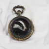 Closed locket casing with badger embroidery hidden inside.