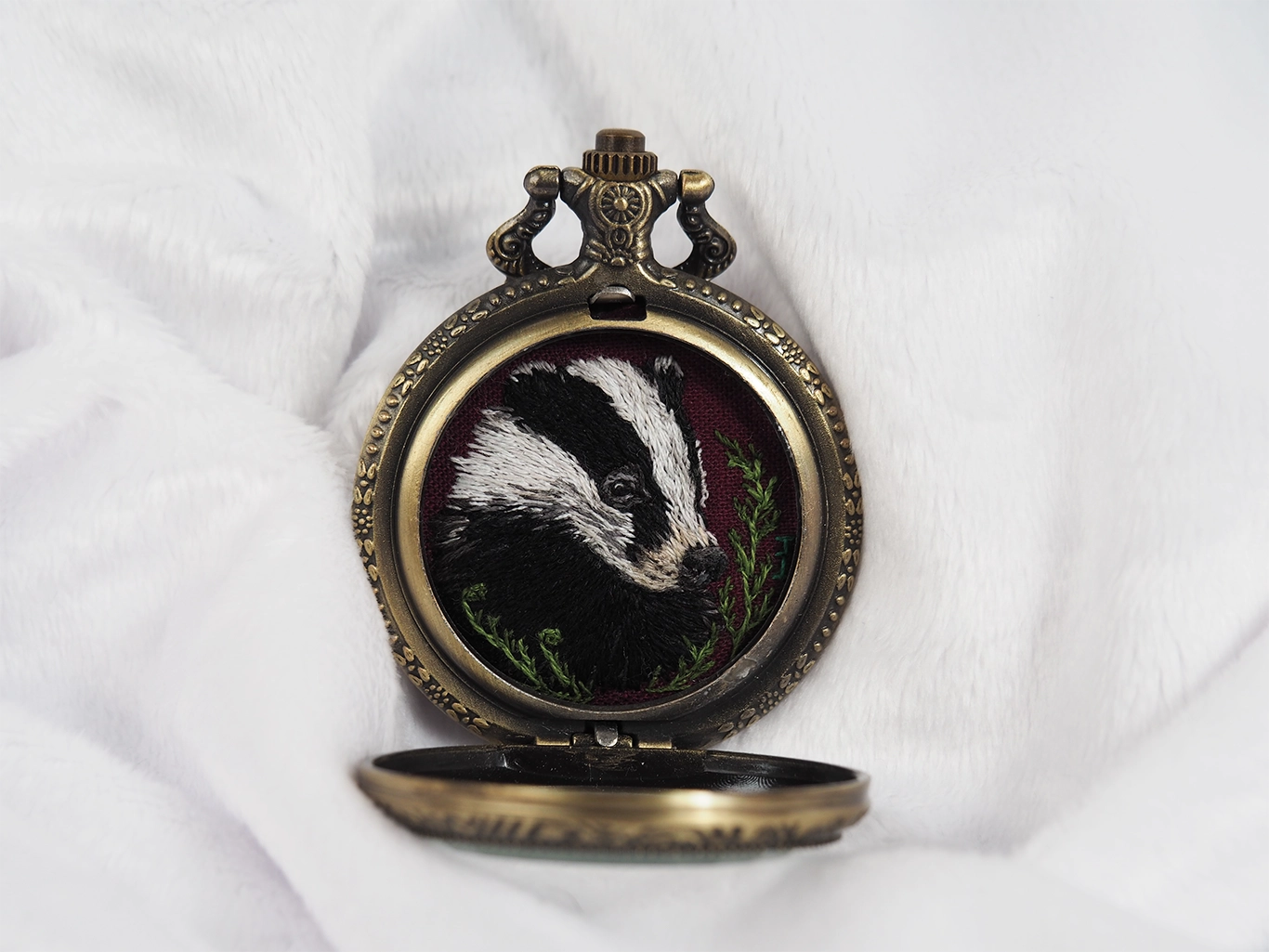 Badger portrait hand-embroidered inside an open locket, front view.