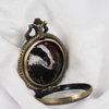 Side view of open locket showing embroidered badger.