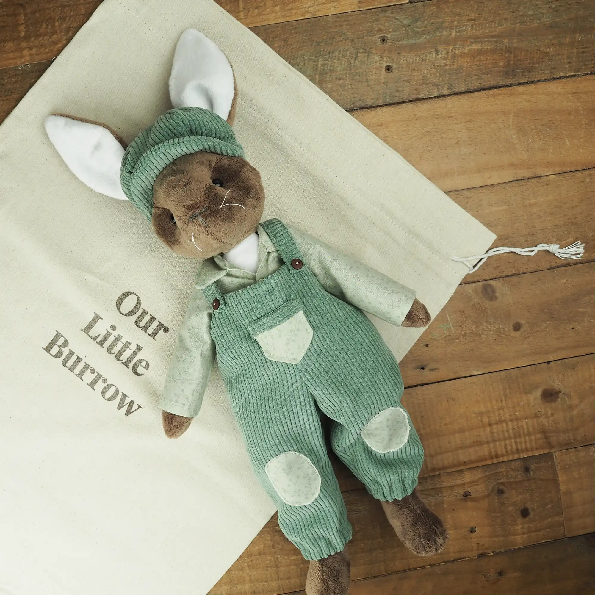 Burrowfolk rabbit, Freddie, laying down on an Our Little Burrow branded cloth bag.