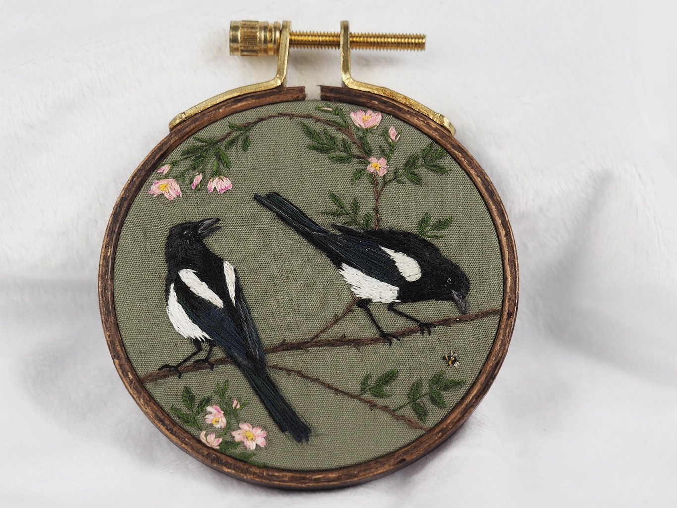 Hand embroidered artwork of two magpies on a branch with roses, in a 3-inch hoop.