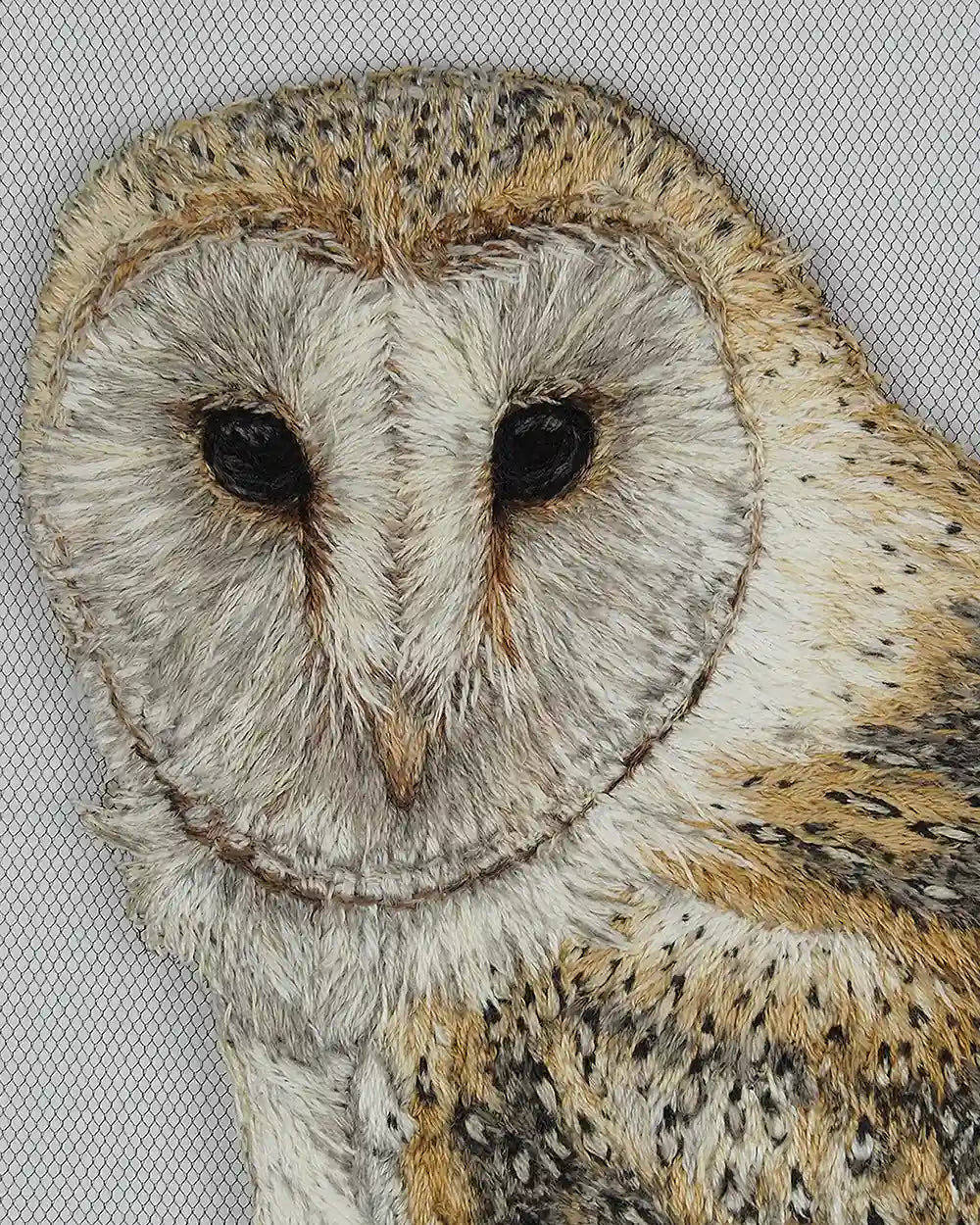 Close-up of embroidered barn owl face in thread painting technique.